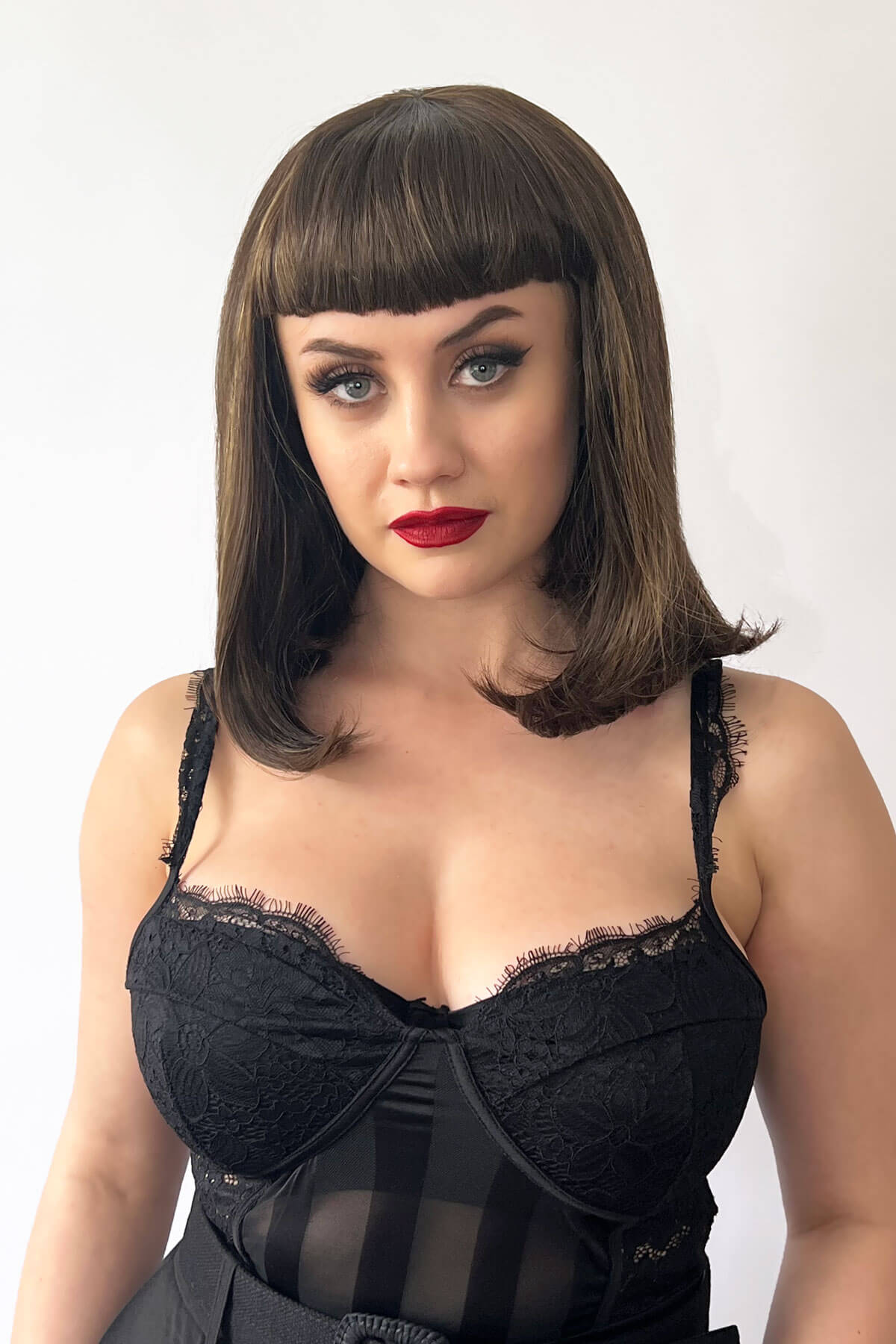 A person wearing a long bob wig with a short fringe, colored in chestnut brown with blonde highlights, styled with the hair falling just to the shoulders. Long bob wig with a short fringe, brown with blonde highlights: Jill