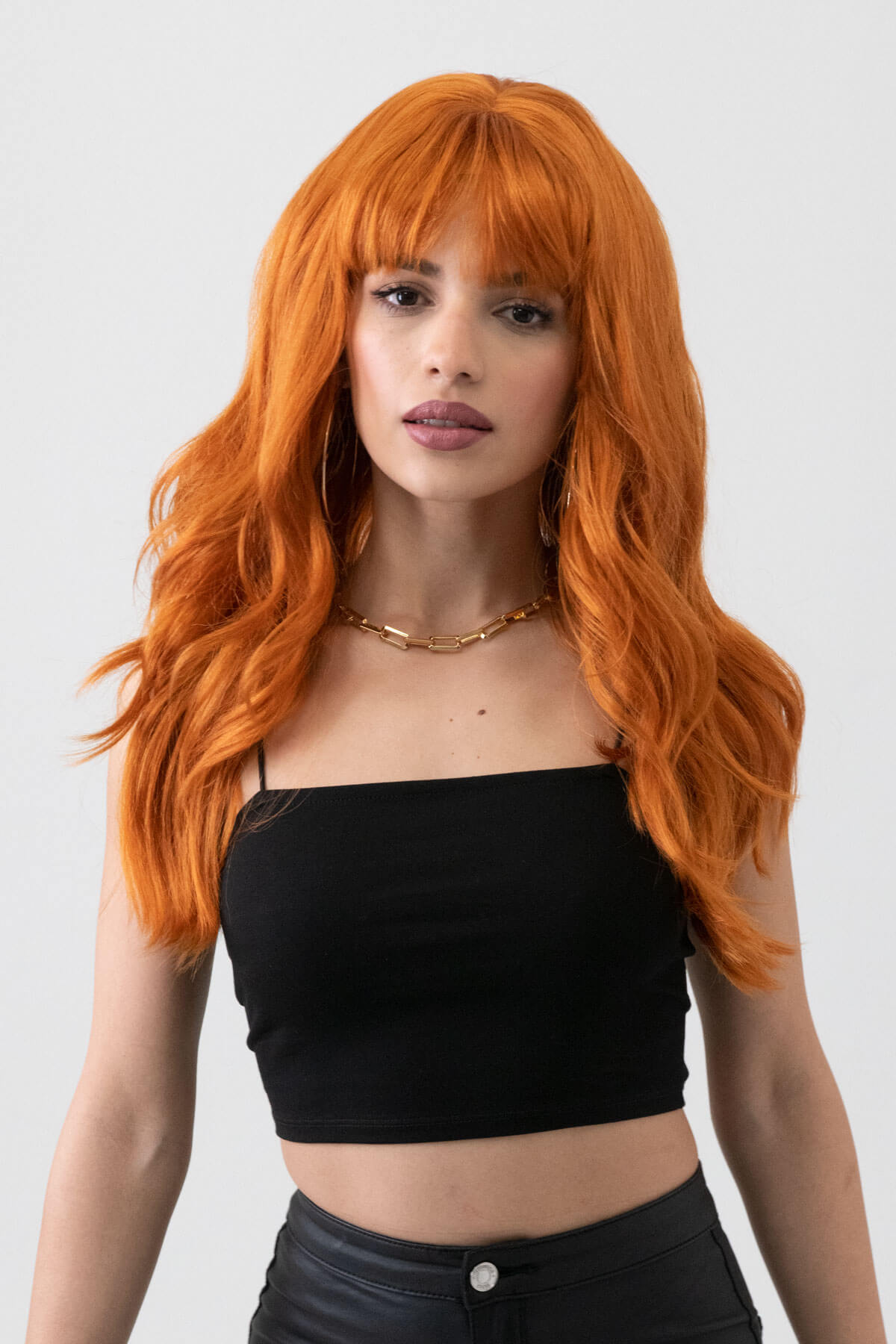 Woman with vibrant orange hair wearing a black top against a plain background. Long ginger wig with cascading waves: Davina