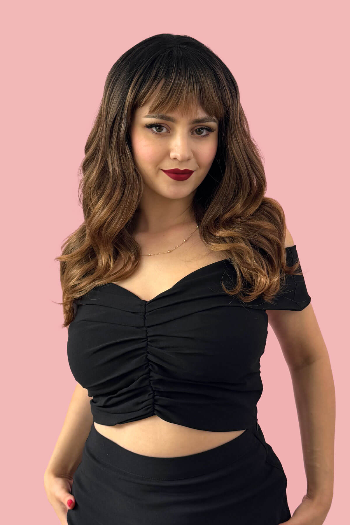 Woman wearing a black top with a pink background. Ombre brown wig with reddish brown highlights & waves: Serenity