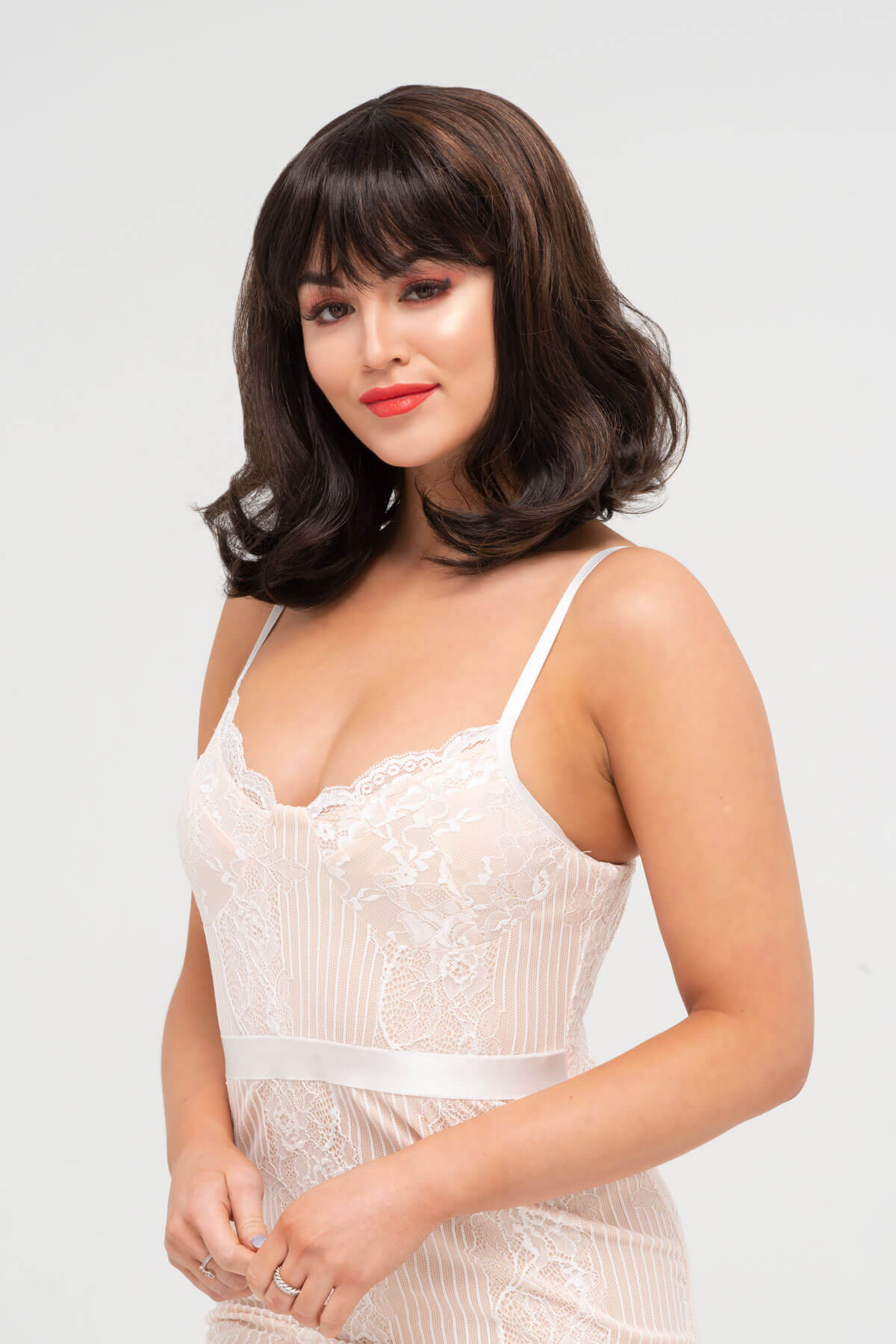 Woman wearing a white lace dress against a plain background. Two tone brown long bob wig with flicked tips: Sheridan