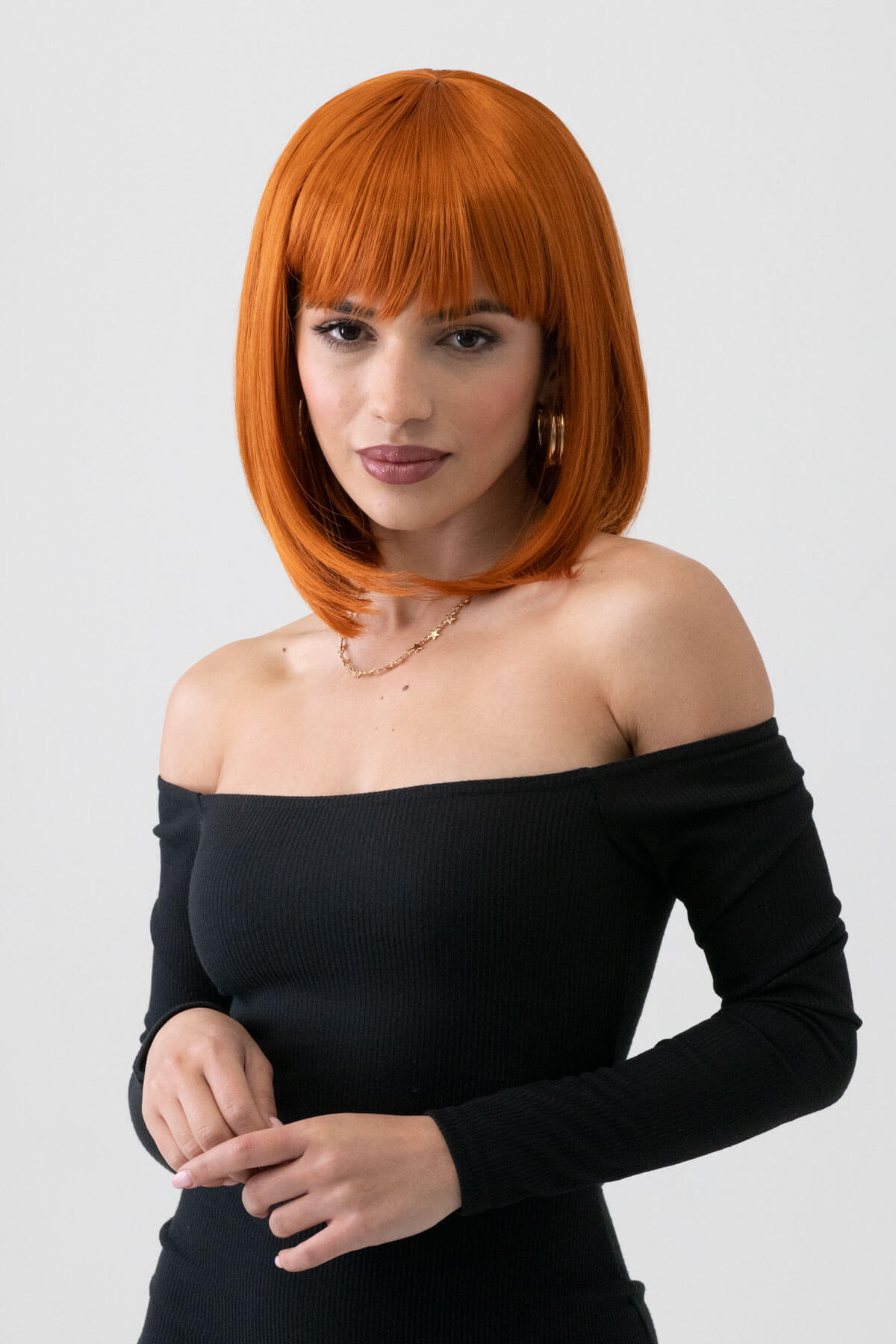 Woman with orange hair wearing a black off-shoulder top against a white background. Ginger bob wig, shoulder length: Ember