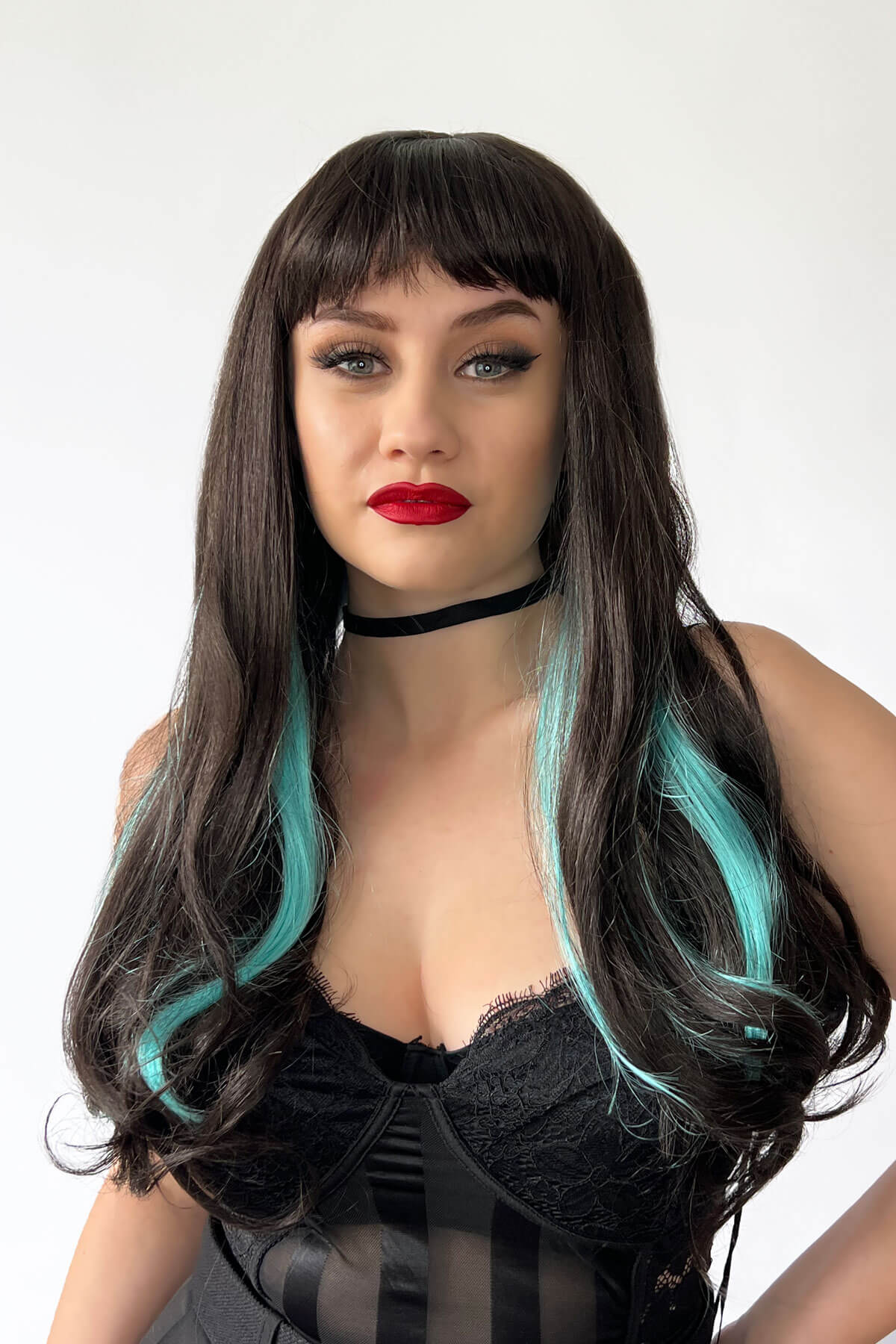 Woman with a black wig with teal highlights wearing a black outfit on a white background. Long dark brown wig with blue streaks and a straight fringe: Cyane