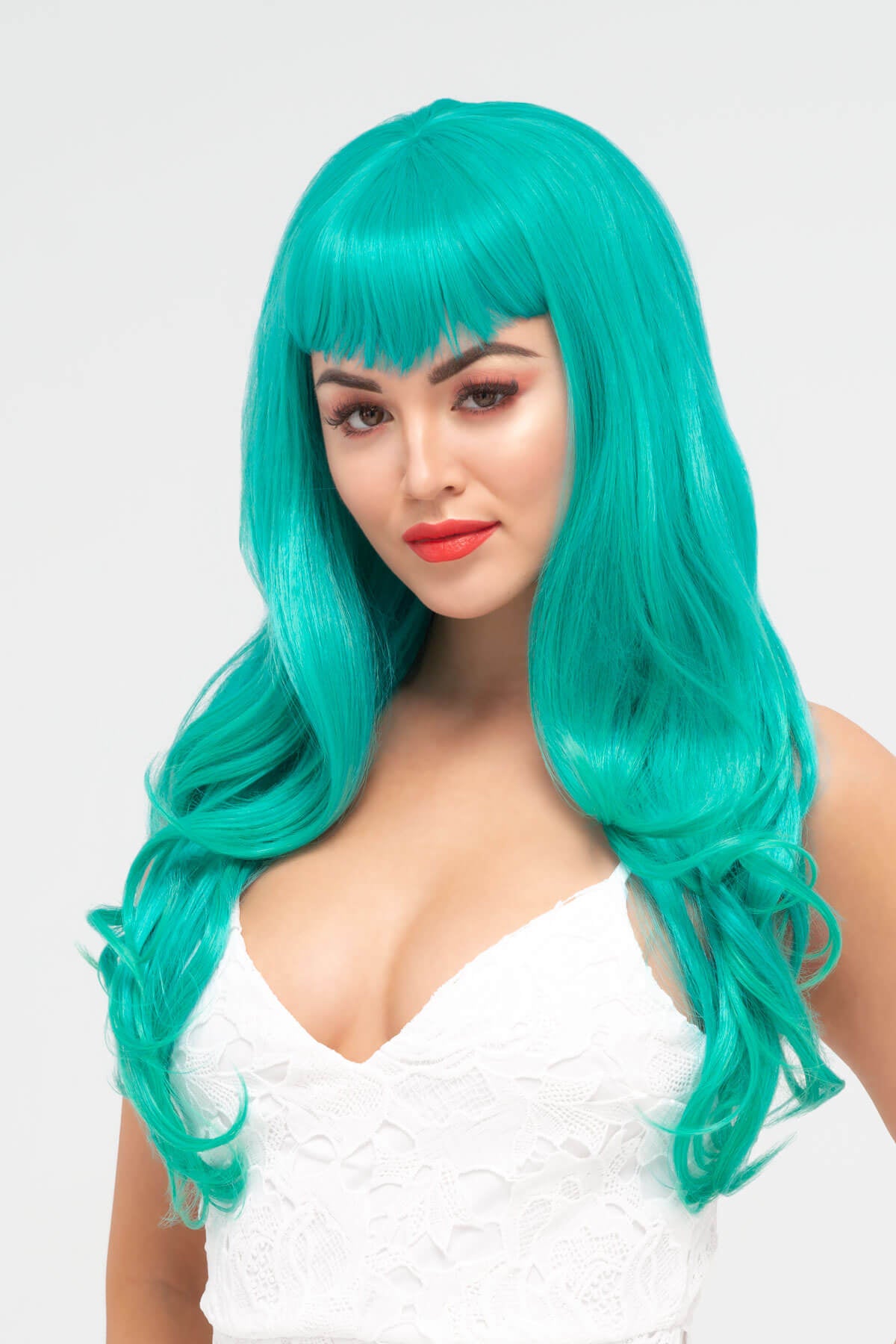 Woman wearing a turquoise wig with bangs on a white background.Long aqua green wig with gentle waves and vintage-style straight fringe: Natalie