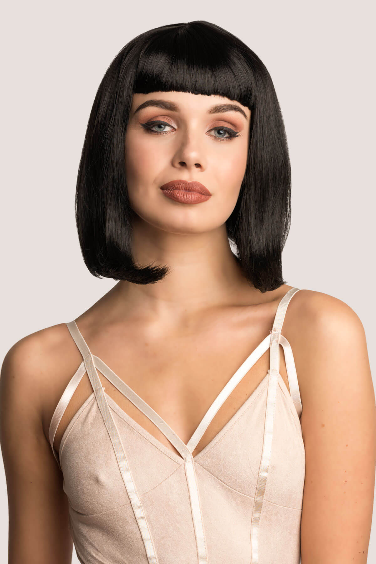 Woman with a stylish bob haircut wearing a beige strappy top on a light background. Black long bob wig with a short retro, rockabilly-style fringe: Beth