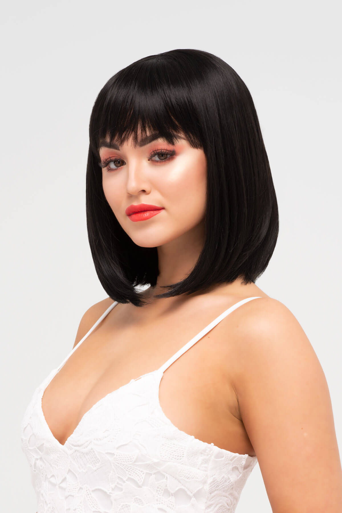 Woman with a stylish black bob haircut and red lipstick against a light gray background. Black long bob wig, shoulder length: Evie