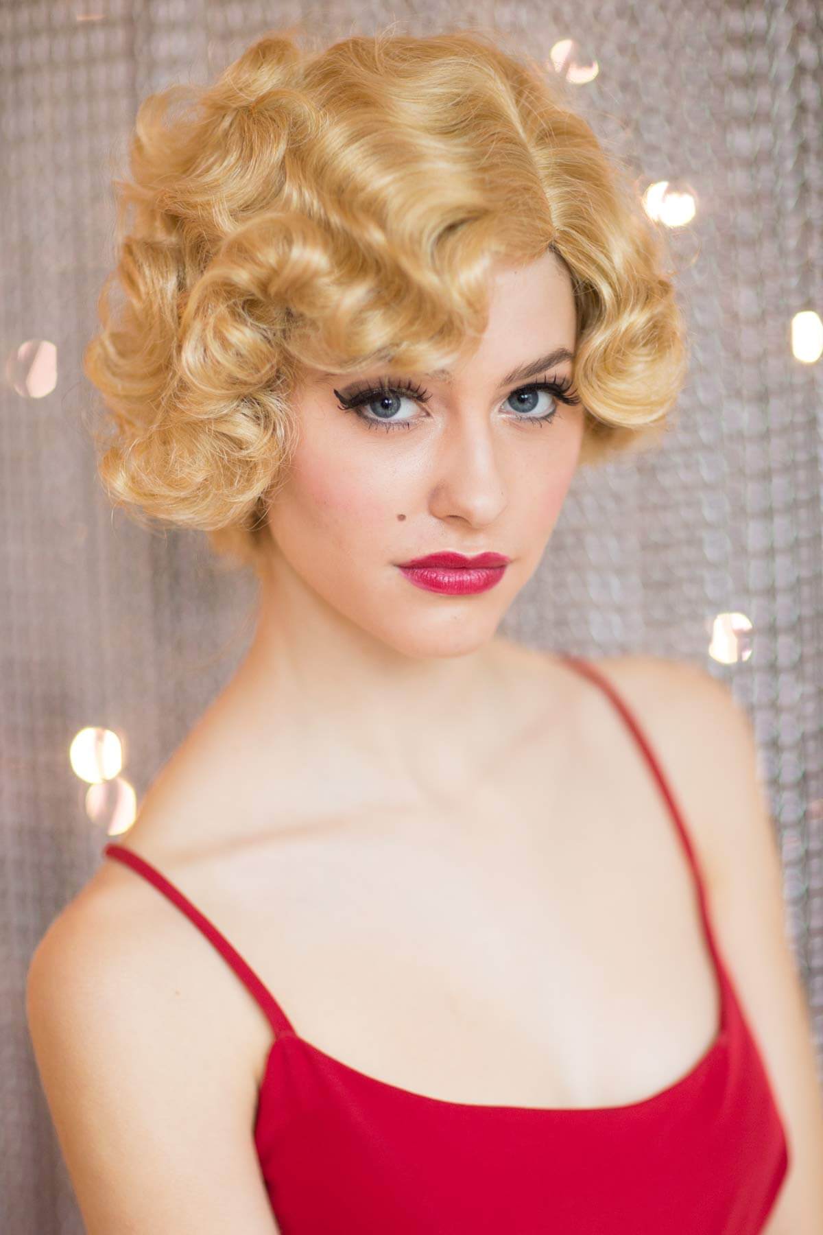 Woman with a blonde wig and red dress against a sparkly background. Blonde 1920s 1930s style wig, short with finger waves: Diva warm blonde 24B