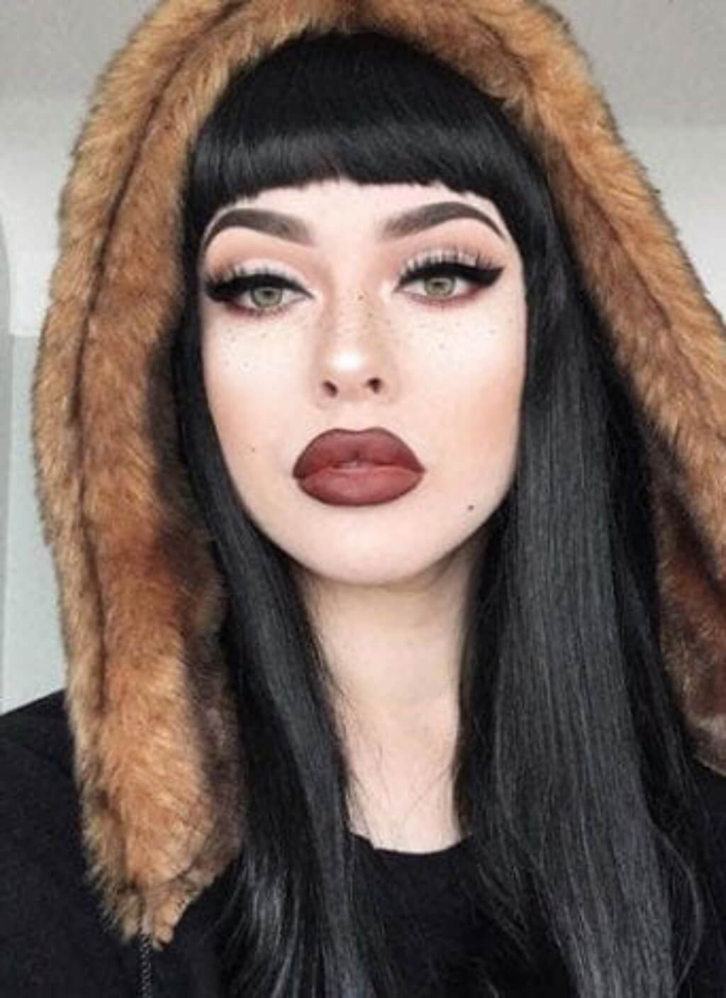 Person wearing a hood with a neutral background. Long straight black wig with straight fringe: Carmen