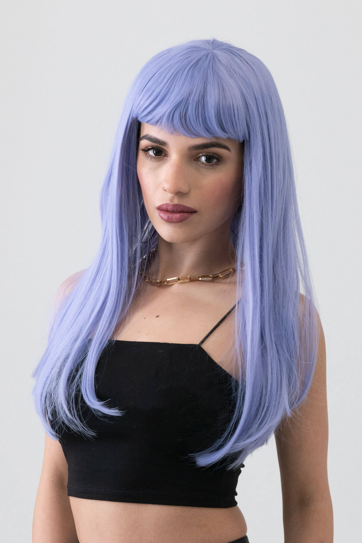Woman with a lavender wig wearing a black top against a plain background. Long blue wig with short, straight fringe: Alyssa