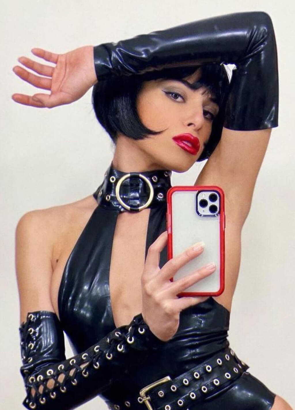 Person in black outfit holding a phone with a white case. Louise Brooks style wig, short black bob: Brooks
