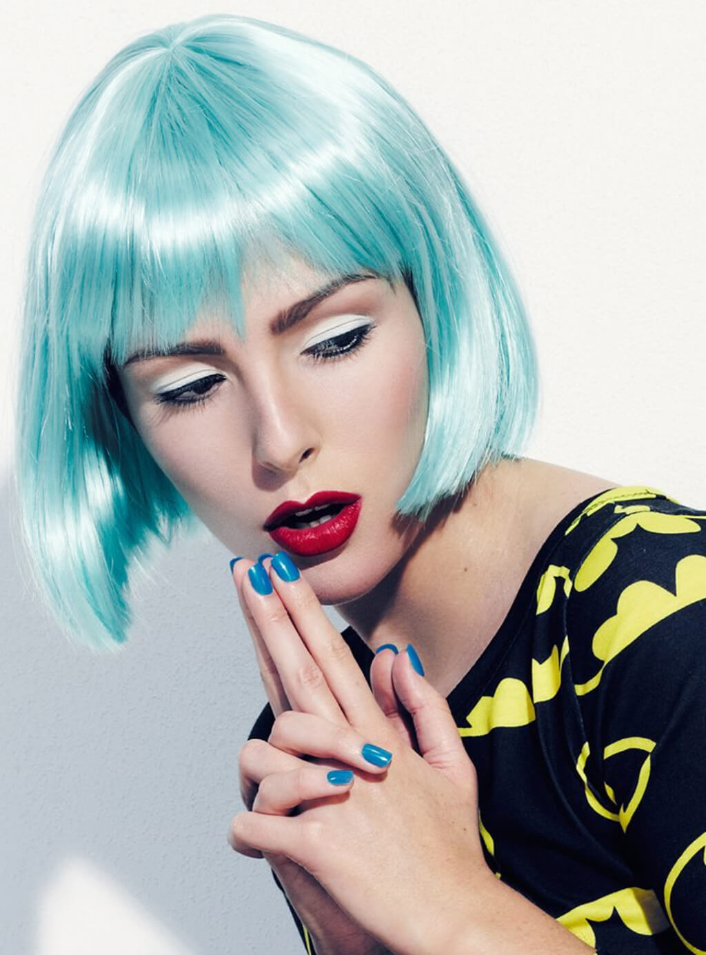 Person with turquoise hair and red lipstick posing against a light background. Turquoise bob wig  with full fringe: Iris