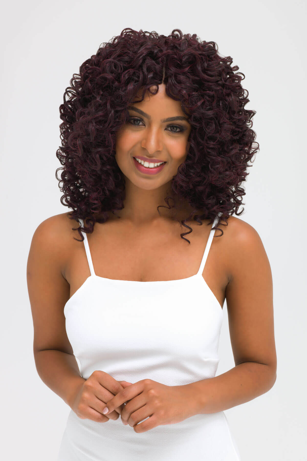 Woman with curly hair wearing a white top on a white background. Afro, corkscrew curly lace front wig, black and purple: Anna