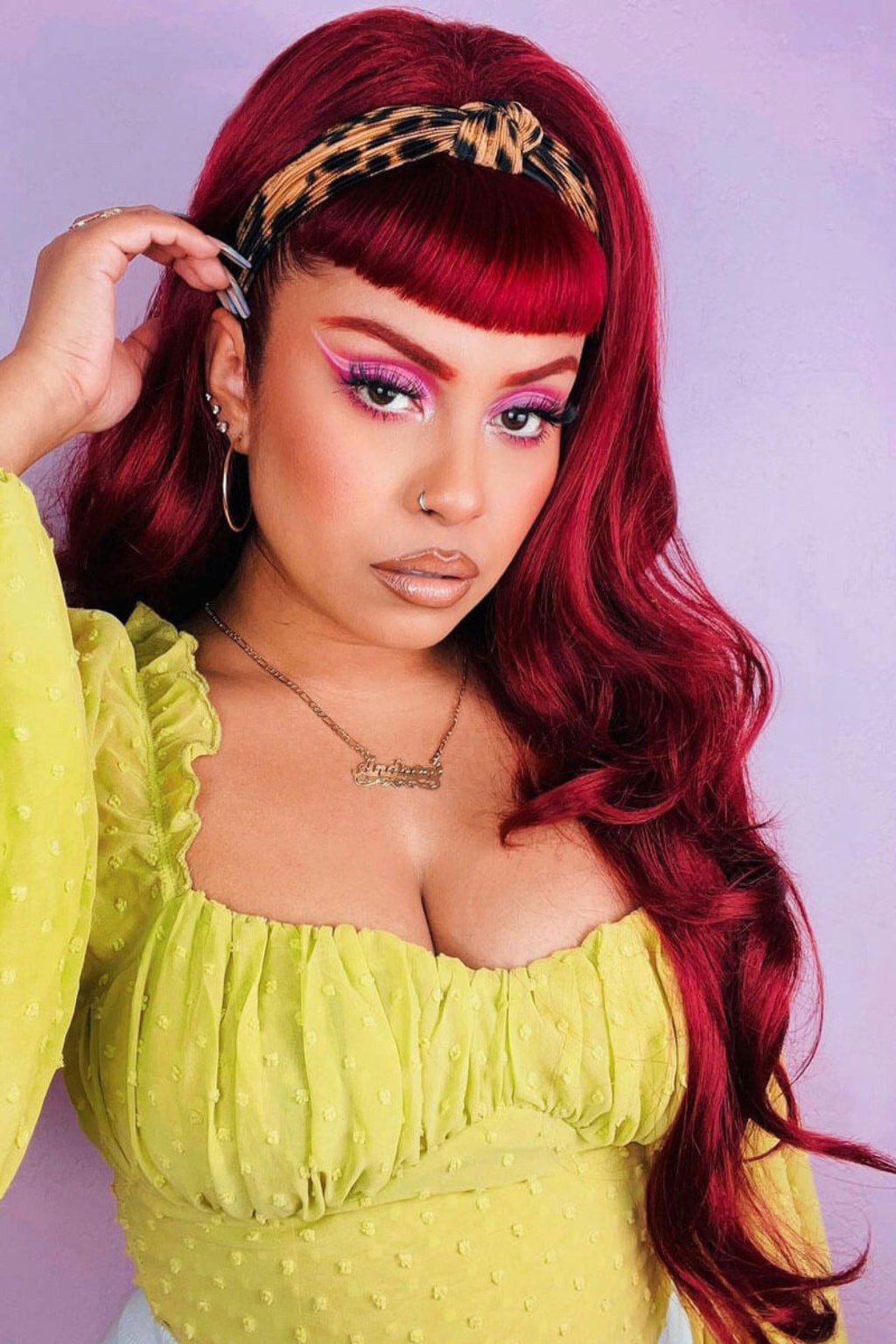 A person with high-crown, long, wavy red hair wearing a green off-shoulder top and a animal print headband.