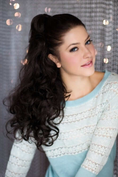 A woman wearing a long wavy ponytail hairpiece extension with loose and layered curls. Long wavy ponytail hairpiece extension: Tiffany